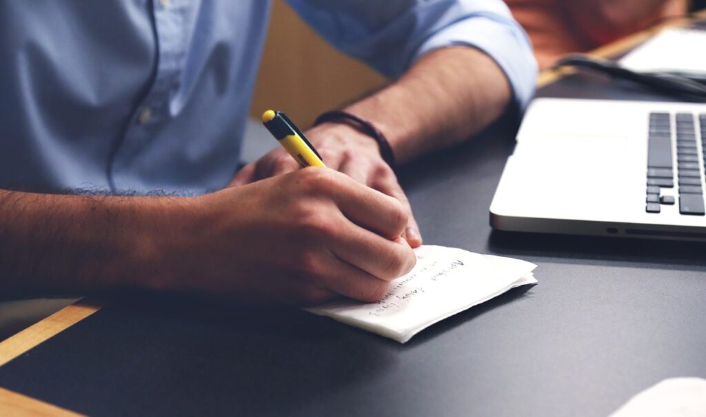 Professionnel en chemise prenant des notes à son bureau à côté d'un ordinateur portable